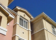 A view looking up at the exterior of White Oak Apartments, showing the pink and beige stucco exterior with large windows and variation in the setbacks of the front walls.